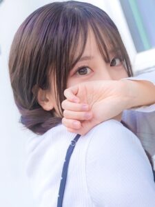 Close-up portrait of a young woman with long hair, resting her forearm over her mouth and looking at the camera.