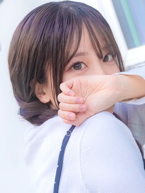Close-up portrait of a young woman with long hair, resting her forearm over her mouth and looking at the camera.