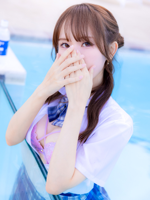 Young woman in a white blouse and plaid tie by a pool, hands raised to her face, looking at the camera.